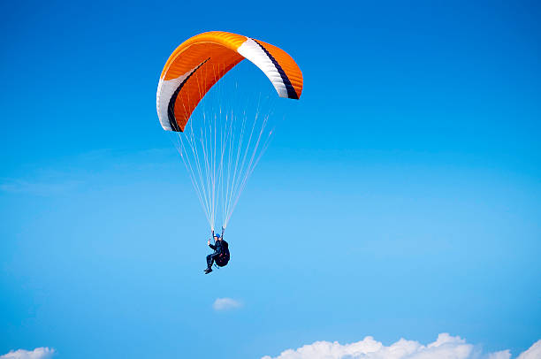 Paraglider, airborne against big blue sky, UK A wide angle view of a paraglider flying high in the sky against a blue background. Space for copy and text. ProPhoto RGB profile for maximum color fidelity and gamut. paraglider stock pictures, royalty-free photos & images