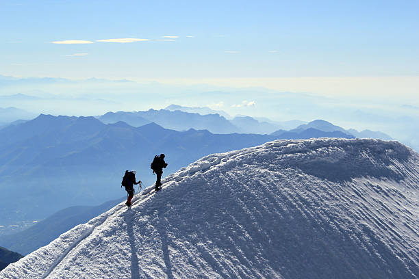 Summit Two mountaineers reach the summit of a 4000m peak in the Swiss Alps. Narrow summit ridge with views to distant mountain ranges. reach destination stock pictures, royalty-free photos & images