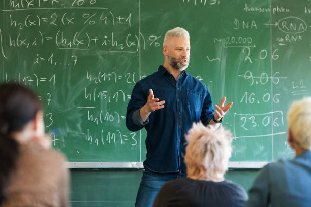 istock Mature teacher standing against blackboard 1830351806
