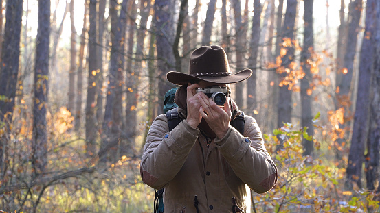 A man in a hat takes pictures in the forest