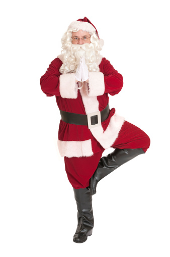 Santa standing in a yoga tree pose, destressing in preparation for the hectic season ahead.   Isolated on white.