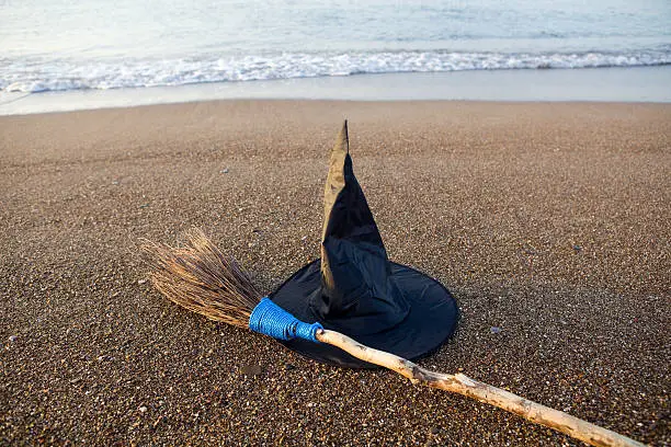 Photo of Witch's Hat And Broom On Beach Sand By Sea Vawes