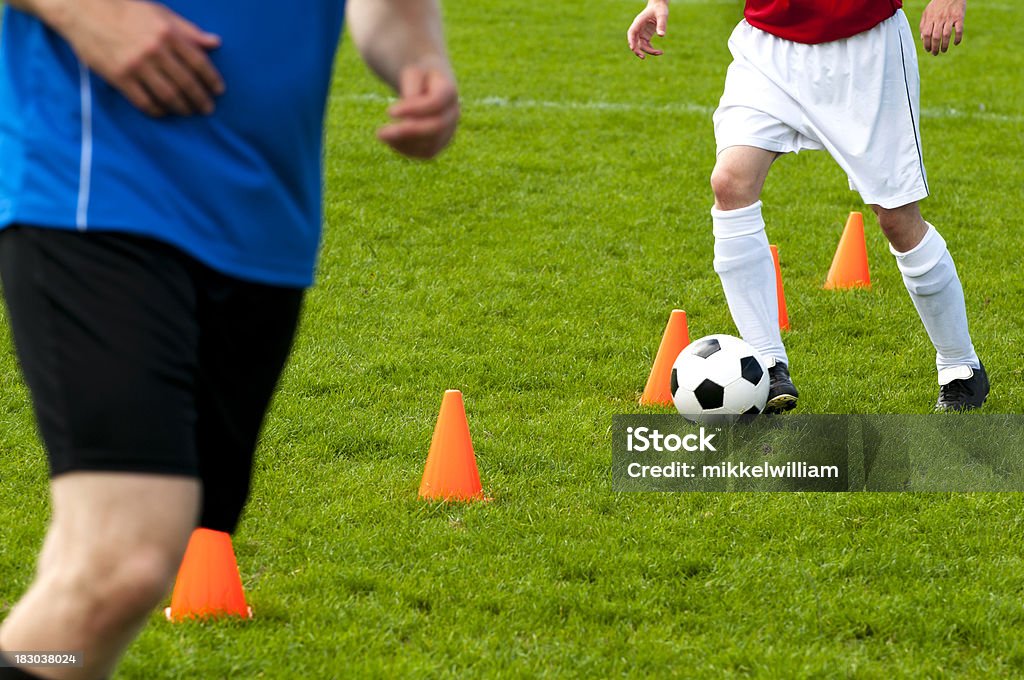 Soccer players warm up and run past cones with ball Soccer players running past red cones on soccer field. Warm up or pratice Cone Shape Stock Photo