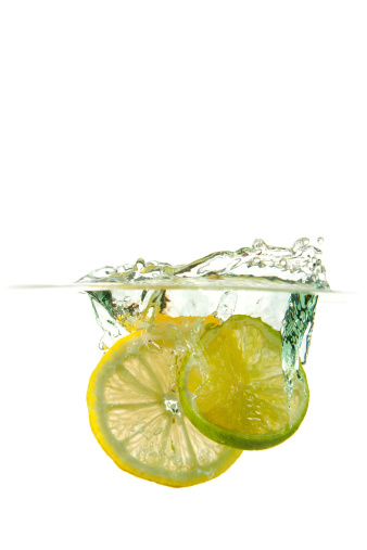 Fresh slices of lemon and lime splashing into clear fresh water.