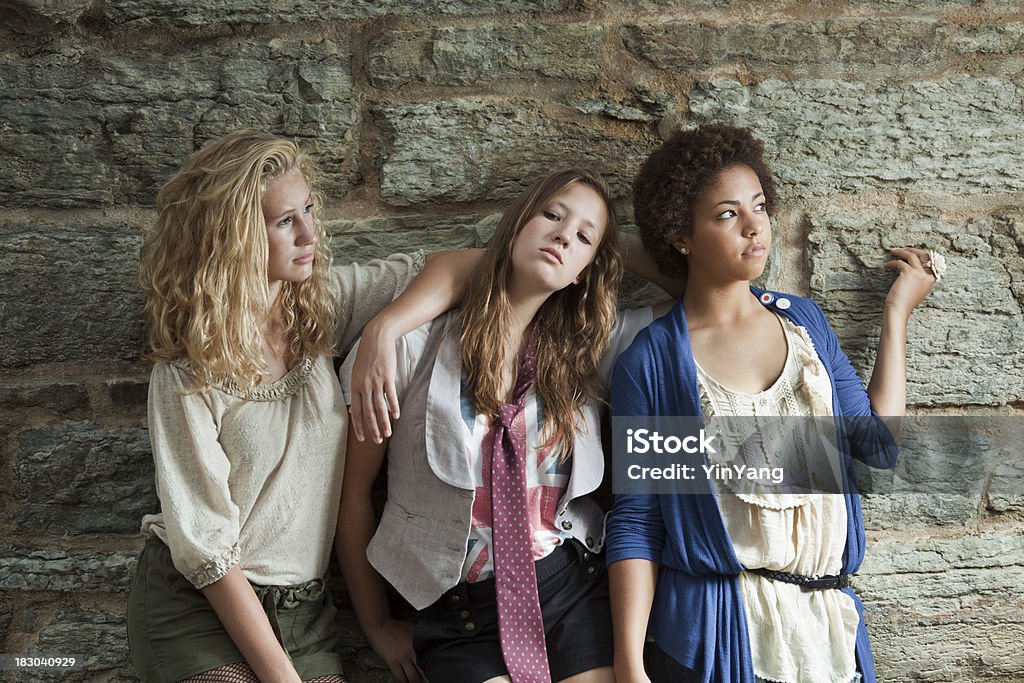 Mujeres jóvenes: Three Teenage Girls mirando tonos by Stone Wall - Foto de stock de Chica adolescente libre de derechos
