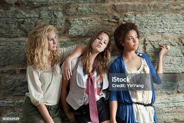 Mujeres Jóvenes Three Teenage Girls Mirando Tonos By Stone Wall Foto de stock y más banco de imágenes de Chica adolescente