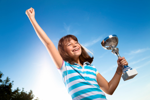 Little girl lifting a trophy,sunburst and blue cloudy sky . Saturated