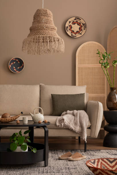 istock Creative composition of boho living room interior with beige sofa, black round coffee table, boho lamp, partition wall, plaid, colorful basket on wall and personal accessories. Home decor. Template. 1830409934