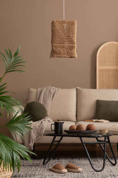 istock Creative composition of boho living room interior with beige sofa, black round coffee table, boho lamp, partition wall, plaid, colorful basket on wall and personal accessories. Home decor. Template. 1830409951