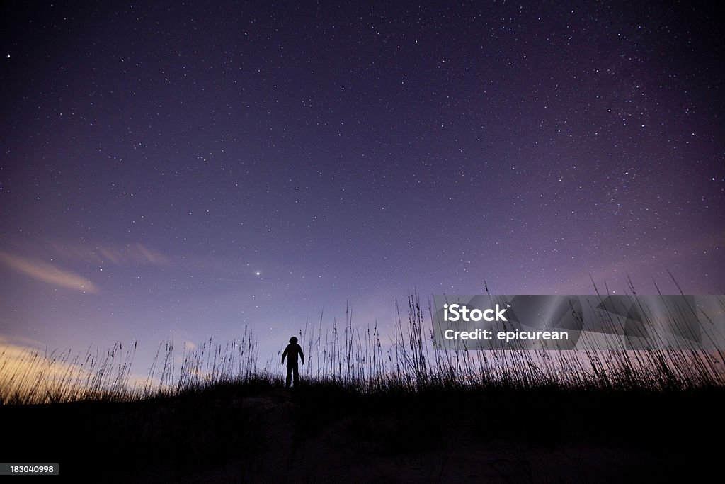 Silhouette of a boy admiring the purple sky. A solitary figure giving thanks under a beautiful night sky of bright stars. Looking Up Stock Photo