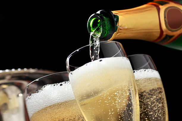 Champagne being poured into champagne glasses Champagne is being poured into several champagne glasses. The glasses sit in front of the ice bucket that held the champagne bottle as bubbles from the freshly poured champagne can be seen.  The camera is tilted slightly of axis.   champagne stock pictures, royalty-free photos & images