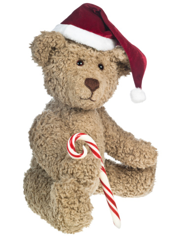 A brown Christmas teddy bear on a white background sitting. Teddy bear is holding a red and white candy cane and has a red santa hat on.