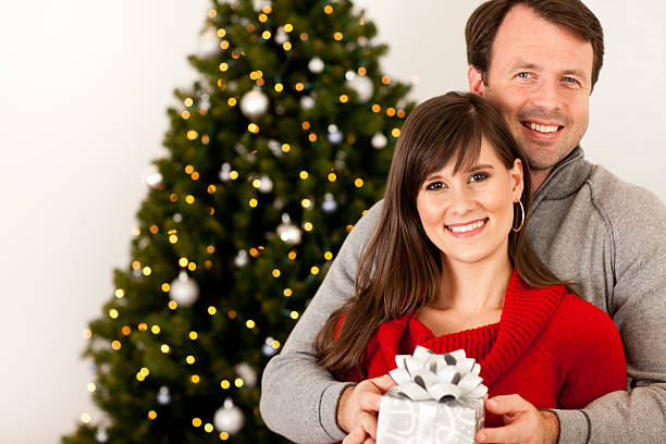 istock Happy Couple Holding Gift by Christmas Tree and Lights 183044776