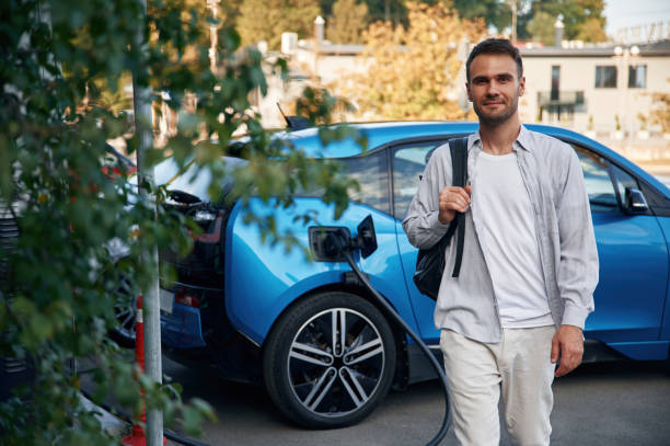 istock With backpack. Man with blue electric car on the charge station 1830449642
