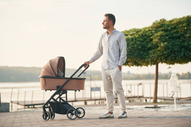 istock Green tree behind. Young father is outdoors, standing with pram 1830462392