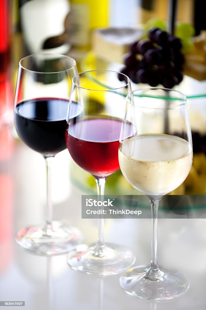 Cheese, grapes and 3 glasses of wine in different colors Three wineglasses with different colors of wine, some grapes and cheese on white and blurred background with wine bottles Red Stock Photo