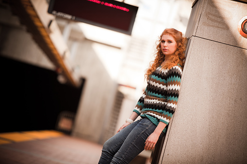 A girl leans on a wall and looks at the camera as she waits for a Bay Area Rapid Transit (BART) train to arrive