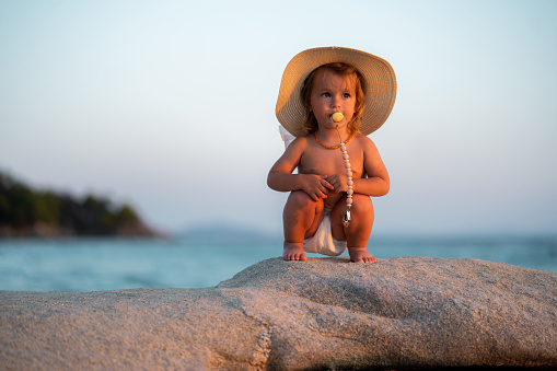 Cute little girl whit sun hat and pacifier at the beach