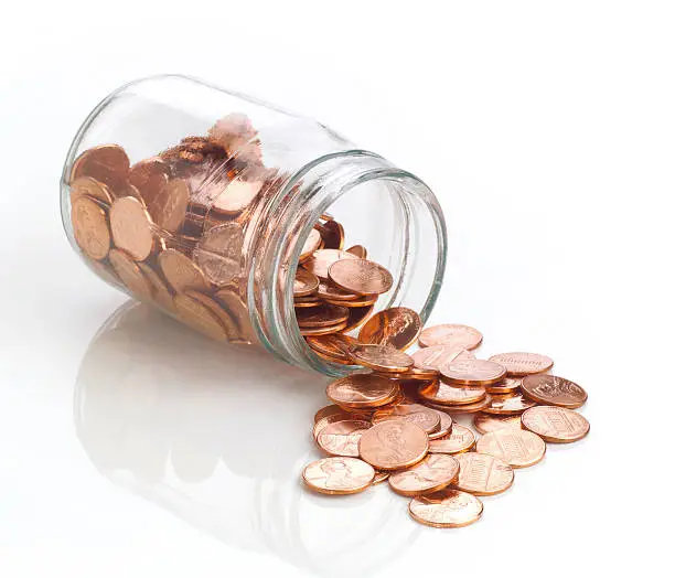 Photo of Jar of polished US pennies spilling out on white