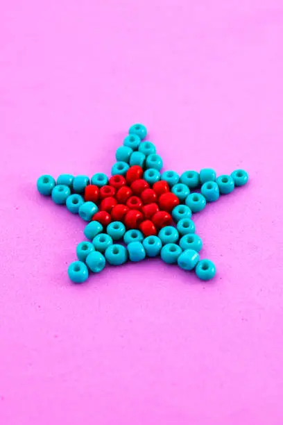 Photo of Star formed with red and greenish blue beads on pink background