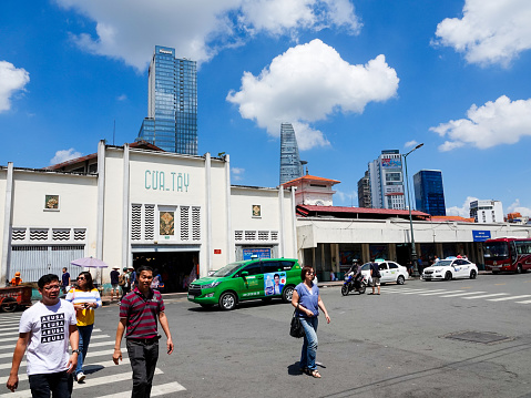 Ho Chi Minh City, Vietnam- September 9, 2018:Pedestrians crossing in front of Ben Thanh Market with modern skyscrapers behind.