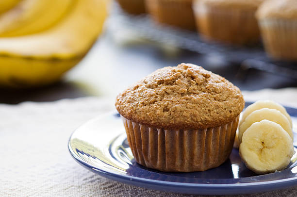 Banana Bran Muffin A banana bran muffin sits in front of bananas and other muffins. cooked selective focus indoors studio shot stock pictures, royalty-free photos & images