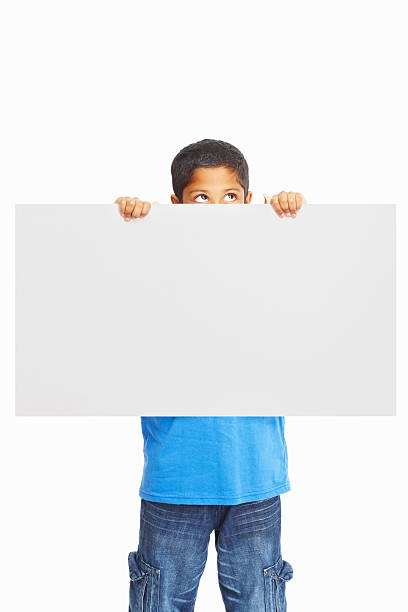 istock Casual boy holding blank board and looks up against white 183049569