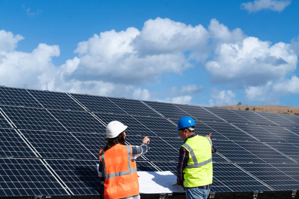 istock Young engineer inspect installation of solar panels installed check  with blueprint on the field, with recording inspection data on pc. 1830507345