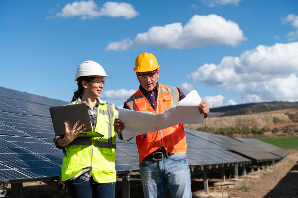 istock Young engineer inspect installation of solar panels installed check  with blueprint on the field, with recording inspection data on pc. 1830519559