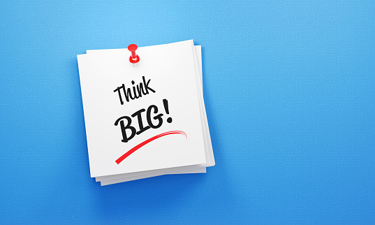 Think big written post its notes pinned by a red thumbtack on blue background. Horizontal composition with copy space. Reminder concept.