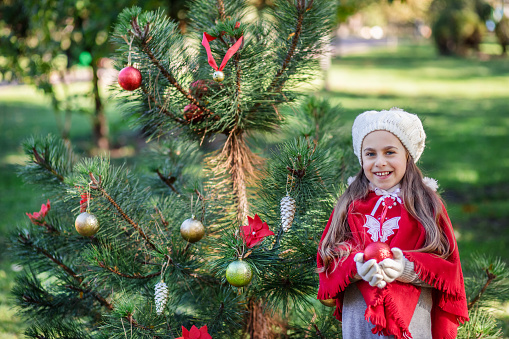 Cute girl decorating the Christmas tree outdoors in the yard before the holidays. Merry Christmas and happy holidays.