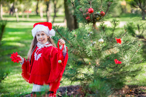 Cute girl decorating the Christmas tree outdoors in the yard before the holidays. Merry Christmas and happy holidays.