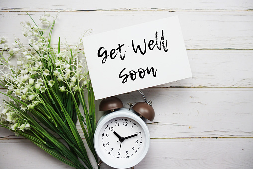 Get well Soon text message with alarm clock top view on wooden background