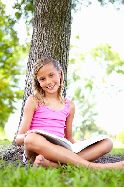 istock Cute smiling girl sitting with a book under the tree 183053454