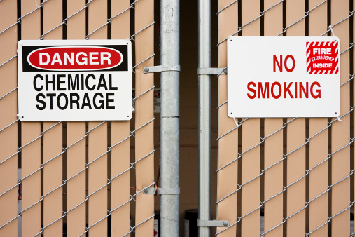 No Smoking and hazardous chemicals signs on chain link fence surrounding chemical storage area.