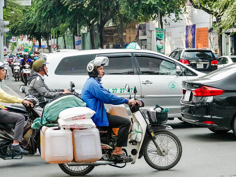 Ho Chi Minh City, Vietnam- September 10, 2018: Scooter rider carrying large gasoline containers on a scooter in busy Ho Chi Minh City traffic.