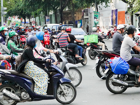 Ho Chi Minh City, Vietnam- September 10, 2018:Woman on a long dress riding in crowd of scooters on a busy Ho Chi Minh City street.