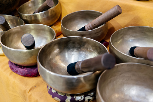 Traditional Tibetan singing bowls on a vibrant yellow fabric, each with a wooden mallet resting inside or beside it. Sound healing therapies, meditation sessions, and spiritual rituals.