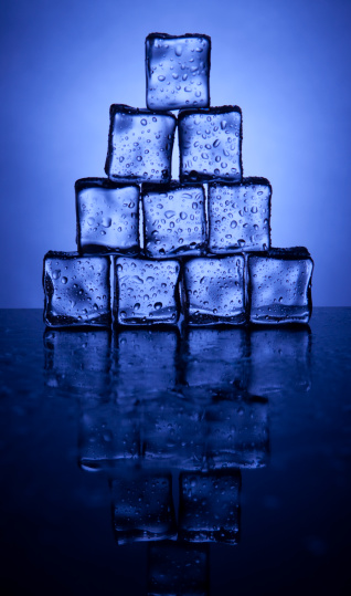 Pyramid of sweating ice cubes against blue background. With reflection.