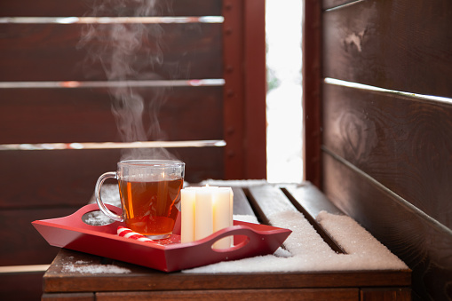 cup of tea with burning candle in snow on balcony in winter