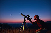 Astronomer looking at the starry skies and crescent Moon with a telescope.