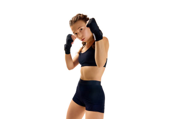 Professional female boxer in action, landing direct hit during training, emphasizing skill and dedication on spotless white studio background. Concept of sport, active lifestyle, health, competition.