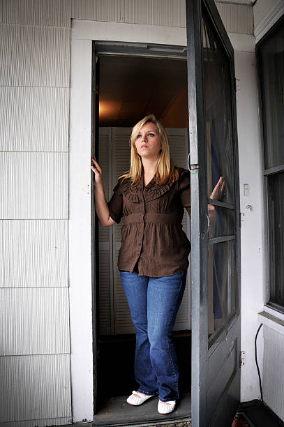 Woman Opening Her Apartment Door Woman opening the screen door of her apartment. She looks out towards a new arrival approaching her entry. She looks a bit sad/serious. looking out front door stock pictures, royalty-free photos & images