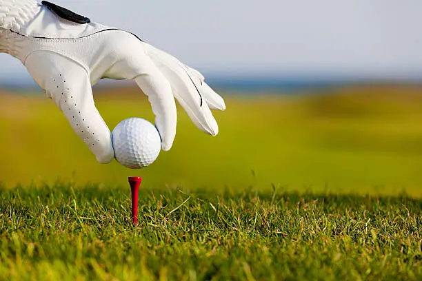 Man's hand placing a golf ball on the tee prior to teeing off.