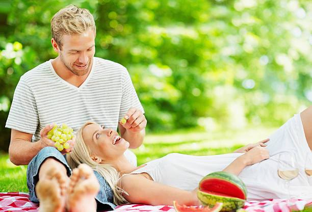 Loving middle aged man feeding a woman grapes at picnic Portrait of a loving middle aged man with woman feeding her grapes at a picnic feeding grapes stock pictures, royalty-free photos & images