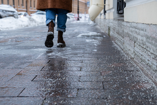 Selective focus on technical salt grains on icy sidewalk surface in wintertime, used for melting ice and snow. Applying salt to keep roads clear and people safe in winter weather from ice or snow