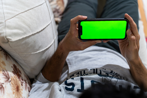 Male model holding a cell phone. Phone with green screen. The man using the phone in the living room of the house.
