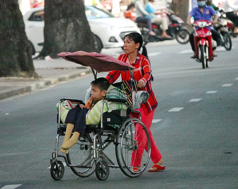 Ho Chi Minh City, Vietnam-September 10, 2018: Woman wheeling a child in a wheelchair across a street.