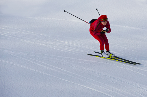 A female cross-country skier takes a turn on a downhill at the Canmore Nordic Centre Provincial Park in Alberta, Canada. She is doing the skate skiing, or freestyle technique, and is using skate skiing equipment.