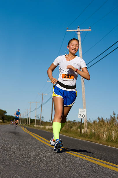 mulher correndo uma corrida em uma estrada usando calções azuis - distance running audio - fotografias e filmes do acervo